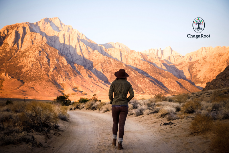 Woman in a hat walking a desert trail toward red mountains