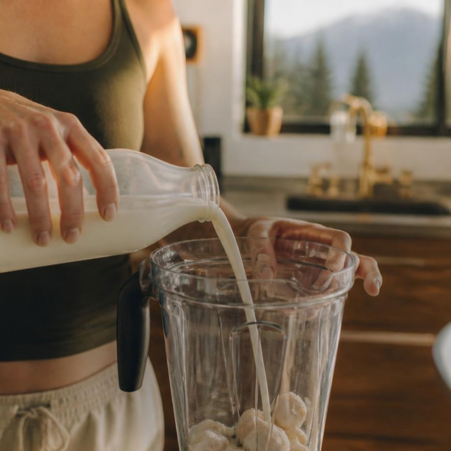 Milk being poured into a blender with frozen banana for a smooth protein shake